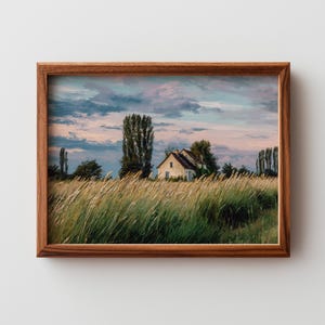 May include: A framed landscape painting depicts a rural scene with a small house, tall grasses, and trees under a cloudy sky. The artwork is encased in a brown wooden frame, enhancing the naturalistic aesthetic. The color palette includes greens, yellows, blues, and pinks.