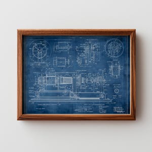 May include: A framed blueprint of a machine, featuring detailed technical drawings in white against a blue background. The wooden frame surrounds the blueprint, showcasing intricate mechanical components and diagrams.
