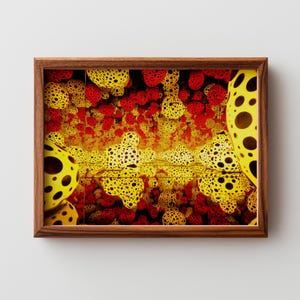 May include: A framed print featuring an abstract design with yellow, red, and black spotted shapes. The artwork has a repeating pattern of organic forms, creating a visually dynamic composition. The frame is made of wood.