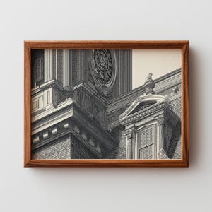 May include: A framed black and white architectural print. The print features a detailed illustration of a building with a large clock, brickwork, and ornate architectural details. The frame is made of wood.