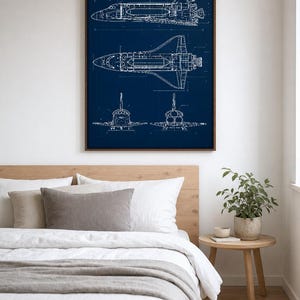 May include: A framed wall art print featuring a white technical blueprint of a space shuttle on a dark blue background. The illustration displays the shuttle from side, top, front, and rear perspectives with detailed lines and engineering markings.
