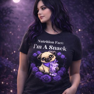 May include: Black t-shirt with the text "Nutrition Fact: I'm A Snack". The shirt features a cartoon pug wearing a bandana and holding a purple drink, surrounded by purple roses. The background is a blurred purple.
