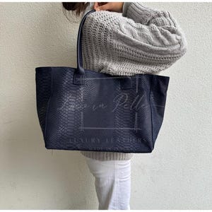 May include: A navy blue tote bag with a snakeskin pattern. The bag has two handles and a rectangular shape. The words "Luxury Leathers" are visible at the bottom of the bag.