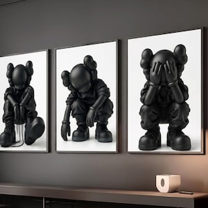 May include: A set of three framed art prints. Each print displays a black sculpture of a figure in different poses, set against a white backdrop. The sculptures have a unique cartoon style, with large, rounded ears. The frames are black.