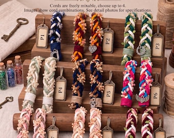 May include: Custom wedding handfasting cords displayed on a wooden stand. The cords are braided in various color combinations, including blue, green, pink, and red, featuring small charms and beads. Metal tags labeled P1 through P9 are attached.