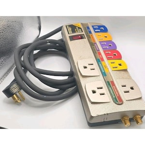May include: A beige and black power strip with multiple outlets and a thick gray cord. The power strip has colored labels and the text "Monster Power". It features a power switch and two coaxial cable connectors.