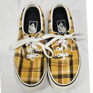 May include: A pair of low-top sneakers featuring a yellow, black, white, and red plaid pattern. The shoes have white laces, white rubber soles, and a black interior lining with the Vans logo printed on the heel area of the insole.