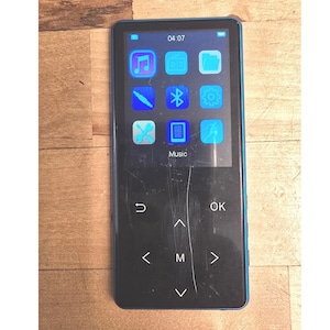 May include: A rectangular blue digital music player with a black screen displaying a grid of light blue icons including music, radio, folder, Bluetooth, settings, and tools. The device features touch-sensitive navigation buttons labeled with arrows, M, and OK.