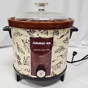 May include: A Hamilton Beach Simmer-On 4 quart slow cooker with a cream-colored exterior featuring a brown botanical print. It has a brown ceramic rim, a clear glass lid, black side handles, and a front control panel with off, low, and high settings.