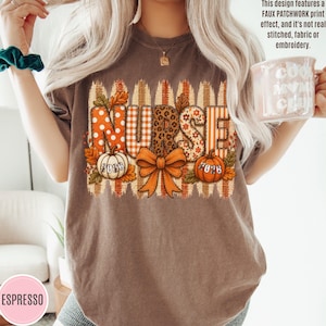 May include: A brown t-shirt featuring a graphic with the word NURSE in a faux patchwork print. The design includes orange and white patterns, a leopard print, a central orange bow, two pumpkins labeled 2026, and autumn leaves.