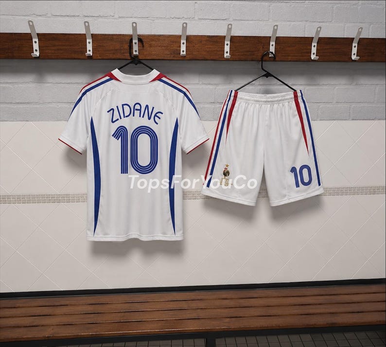 Puede incluir: Un conjunto de camiseta y pantal&oacute;n corto de f&uacute;tbol blanco con detalles en azul y rojo. La camiseta muestra el nombre ZIDANE y el n&uacute;mero 10 en azul. El pantal&oacute;n corto presenta el n&uacute;mero 10 y un peque&ntilde;o emblema. El texto TopsForYouCo es visible.
