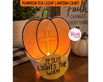 May include: A paper pumpkin tea light lantern craft featuring a central cross cutout and a yellow circular tag with the black text 'JESUS LIGHTS THE WAY!' The pumpkin is colored in shades of orange with a green stem and is illuminated from within.