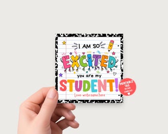 May include: A square tag with a black and white composition notebook border featuring lined paper. The text reads I AM SO EXCITED you are my STUDENT! Love: write name here. Colorful cartoon letters and a yellow pencil graphic are included.