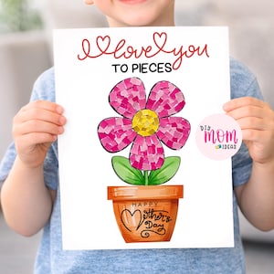 May include: A handmade Mother's Day card held by a child. The card features a mosaic flower in a terracotta pot with the text "I love you to pieces" and "Happy Mother's Day". A pink and white circular logo is in the lower right corner.