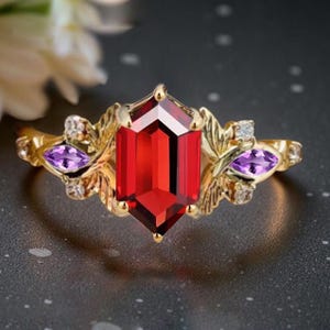 May include: A gold ring with a large, faceted red gemstone at its centre. The ring is decorated with smaller purple gemstones and leaf-like details. Small clear stones are also set into the design.