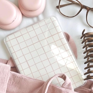 May include: A collection of accessories including a pink corduroy tote bag, a phone case with a grid design, brown spectacles, a hair claw clip, and two pink wireless earbuds, all on a white surface.