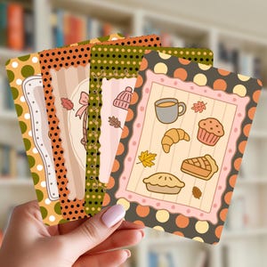 May include: A set of four rectangular cards featuring autumn-themed illustrations. Each card has a polka dot border in shades of orange, green, and brown. The central designs include icons of a coffee mug, croissant, muffin, pie, leaves, and a knit hat.