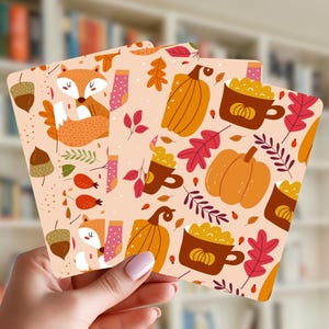 May include: Three rectangular cards featuring a repeating autumn pattern on a light peach background. The design includes orange foxes, yellow pumpkins, brown mugs filled with yellow liquid, acorns, and red and orange leaves in a flat illustration style.