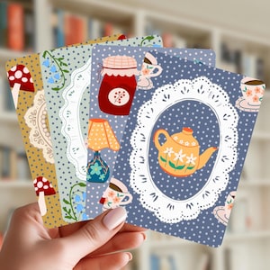 May include: A set of four rectangular cards featuring illustrations of mushrooms, a jam jar, a lamp, and a teapot. Each card has a polka dot background and a white lace-like oval frame. The designs include floral patterns, teacups, and blue flowers.
