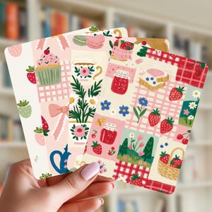 Peut inclure: Un ensemble de trois cartes rectangulaires présentant des illustrations colorées de fraises, cupcakes, tasses à thé, pots de confiture, fleurs et motifs à carreaux dans des tons de rose, rouge, vert et blanc. Les cartes ont des coins arrondis.