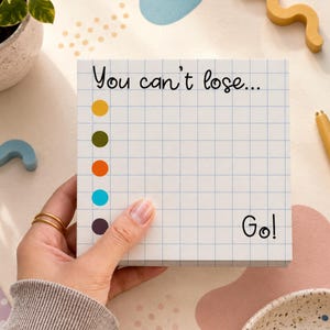 May include: A square notepad with a light blue grid pattern. The top text reads "You can't lose..." and the bottom right text reads "Go!". A vertical column of five colored circles in yellow, olive, orange, cyan, and dark purple appears on the left side.