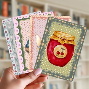 May include: A set of four rectangular cards with rounded corners, featuring decorative borders and illustrations. The front card displays a red jar of cherry jam with a label reading CHERRY, set against a green background with white polka dots.
