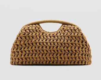 May include: A woven handbag in a light brown hue. The bag features a curved top handle and a rectangular shape with a textured, basket-weave design. The bag is made of a natural fiber material.