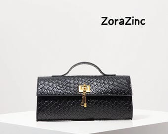 May include: A black rectangular handbag with a woven texture, a single top handle, and a gold-tone metal turn-lock closure featuring a small dangling key charm. The text ZoraZinc is printed in black in the upper right corner of the image.