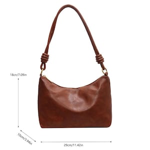 May include: A brown shoulder bag with a curved top and a long strap. The bag is 11.42 inches wide, 7.09 inches tall, and 3.94 inches deep. The strap is attached with gold-colored rings. The bag has a zipper closure.