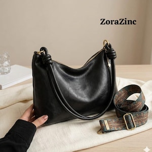 May include: Black leather shoulder bag with a gold zipper and knotted handle. Includes a patterned strap with a gold buckle. The text "ZoraZinc" is visible in the upper right corner.