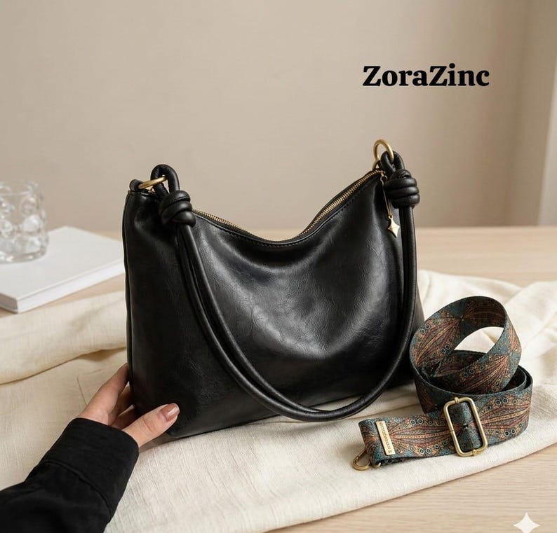May include: Black leather shoulder bag with a gold zipper and knotted handle. Includes a patterned strap with a gold buckle. The text "ZoraZinc" is visible in the upper right corner.