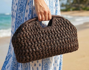 May include: A dark brown woven handbag with a curved top and a handle. The bag has a textured pattern and a leather handle. The bag is held by a person on a beach.