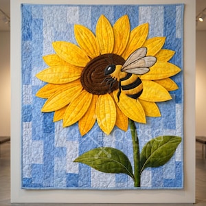 May include: A quilted wall hanging featuring a large yellow sunflower with a brown center and a black and yellow bee. The sunflower is set against a blue and white patchwork background. The quilt includes green leaves and a green stem.