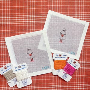 May include: Two square white needlepoint canvases featuring a small ghost character with a red heart and the letters LBN in blue. Four spools of Tilli Tomas essentials silk thread in gray, natural, orange, and pink are included with the canvases.