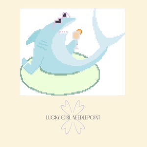 May include: A pixelated illustration of a light blue shark wearing sunglasses and lounging on a green inflatable ring. The shark is holding a cocktail. The text "LUCKY GIRL NEEDLEPOINT" is below the image.