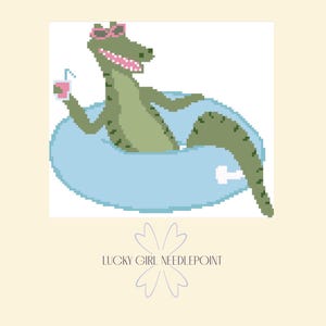 May include: Pixelated illustration of an alligator wearing pink sunglasses and floating in a blue inner tube. The alligator holds a pink drink with a straw. The text "LUCKY GIRL NEEDLEPOINT" is below the image.