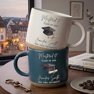 May include: Two ceramic mugs, one white and one teal, stacked. Each mug has the text "Mastered It, Class of 2026" and a graduation cap graphic. The name "Jennifer Smith, New York University" is printed on each mug. A graduation gift.