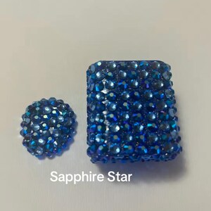 May include: A rectangular case and a separate circular piece, both covered in small, faceted, deep blue crystals that reflect light. The text Sapphire Star is printed in white below the items, which are set against a plain, light-colored background.