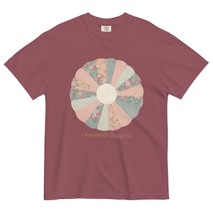 以下が含まれることがあります： パステルカラーの円形キルトデザインが特徴のマルーンTシャツ。キルトパターンには、花柄と水玉模様の生地が含まれています。「Charmingly Vintage Co.」の文字がデザインの下にプリントされています。