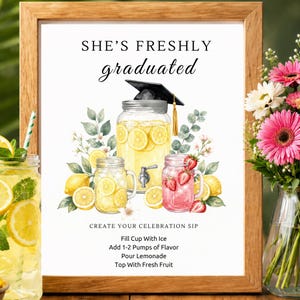 May include: A framed sign with the text "SHE'S FRESHLY graduated" above a watercolor illustration of lemonade and strawberry lemonade in mason jars. The sign includes instructions for making a celebratory drink.