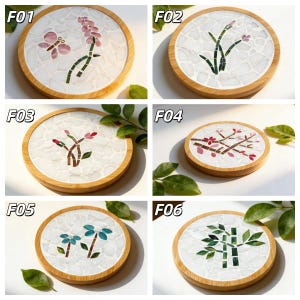 May include: A collection of six round coasters with mosaic designs. Each coaster features a different floral or botanical pattern in various colors, set within a white mosaic background and a natural wood frame. Designs include flowers, butterflies, and bamboo.