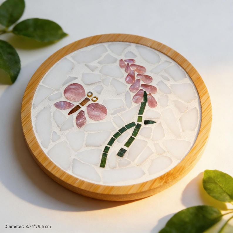 May include: Round coaster with a mosaic design featuring a pink butterfly and flower on a white background. The coaster has a natural wood border and measures 3.74 inches (9.5 cm) in diameter.