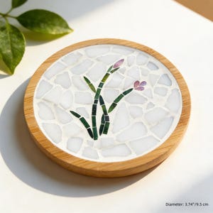 May include: Round wooden coaster with a mosaic tile design. The center features a white mosaic background with a green and purple floral design. The coaster is 3.74 inches (9.5 cm) in diameter.