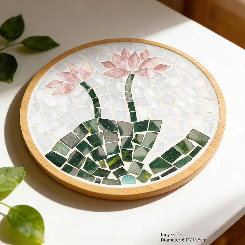 May include: Round mosaic coaster with a wooden frame. The mosaic features two pink lotus flowers with green stems and leaves. The diameter is 6.1 inches.