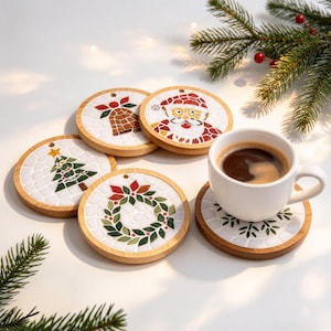 Puede incluir: Cuatro posavasos redondos de madera con diseños navideños estilo mosaico que incluyen una campana, Santa Claus, un pino y una corona. Una taza de cerámica blanca con café negro descansa sobre un quinto posavasos a juego con hojas.