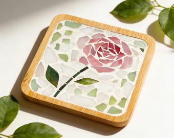 May include: Square coaster with a mosaic rose design. The coaster features a wooden frame and a mosaic tile surface with a pink rose, green leaves, and white and green accents. The coaster measures 3.54" x 3.54" (9x9cm).