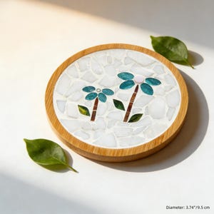 May include: Round coaster with a mosaic design featuring two stylized teal flowers with pink centers and brown stems. The coaster has a wooden border and a diameter of 3.74 inches (9.5 cm).
