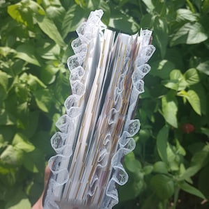 May include: A thick journal with dark brown covers, featuring white lace trim along the edges of the spine. The interior consists of numerous white pages with gold-edged tabs protruding from the side, creating a layered and organized appearance.