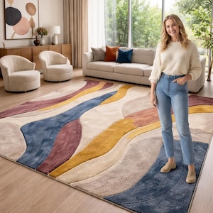 May include: A large, patterned rug featuring flowing abstract shapes in blue, yellow, burgundy, and beige. The rug is in a living room. The rug's dimensions are not visible, but it appears to be a substantial floor covering.