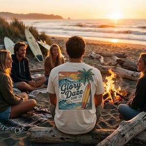 Puede incluir: Escena de playa al atardecer con un grupo de personas alrededor de una hoguera. Una persona lleva una camiseta crema con un gráfico que dice "Glory Daze Surf Co" y presenta una palmera, una tabla de surf y olas.